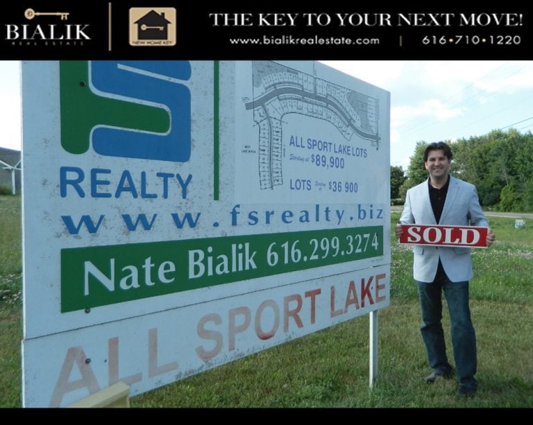 A man holds a SOLD sign beside a Sport Lake lots real estate sign.