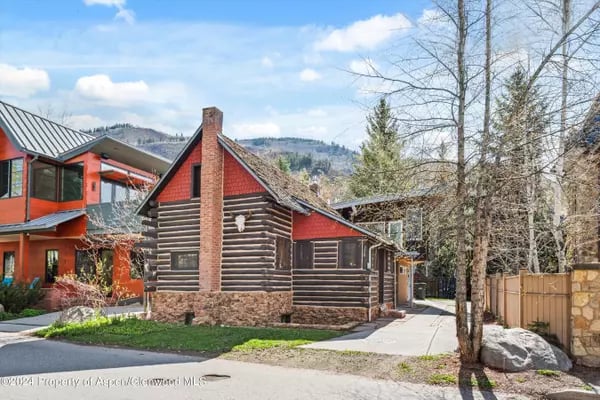 Rustic log-sided home with red gable accents and stone foundation beside a modern red-orange house.