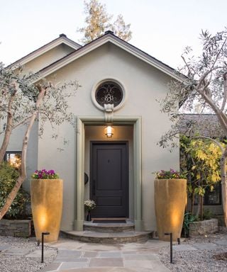 House entrance with a circular window above a dark door and tall planters flanking the stone path.