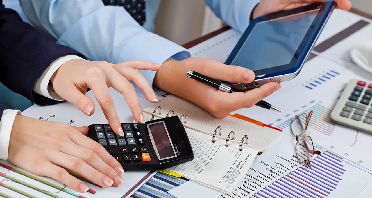 Hands using a calculator and tablet to review financial charts and paperwork