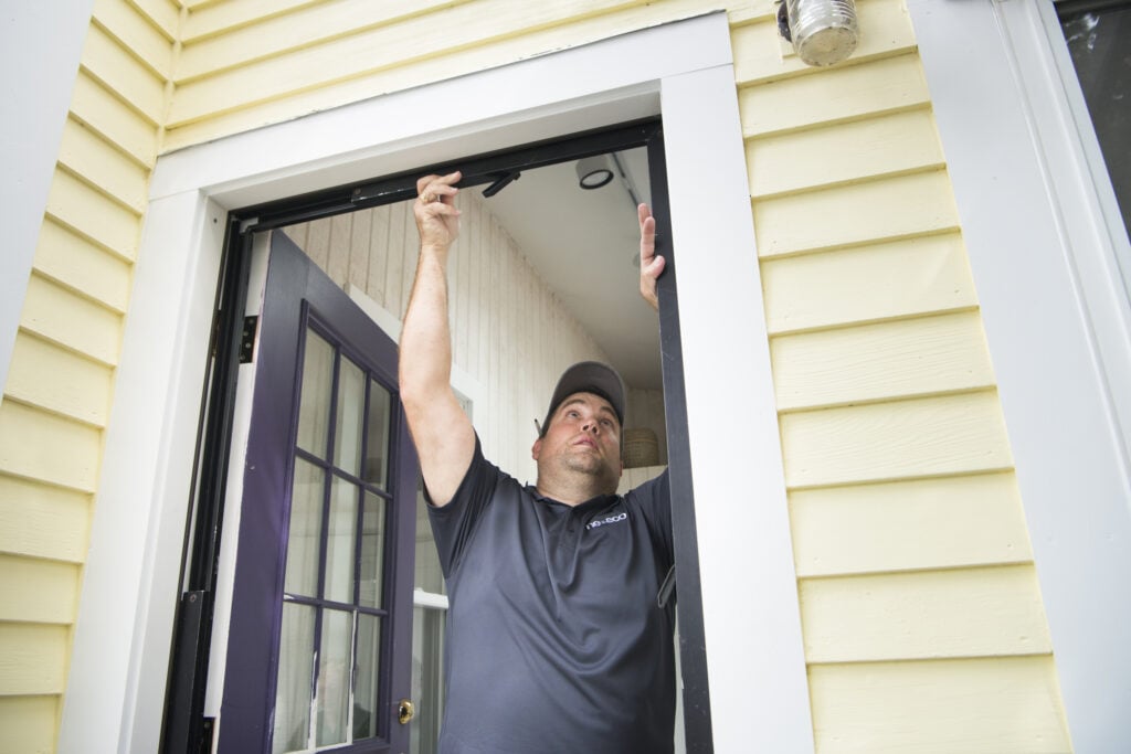 Worker adjusts the frame of an exterior doorway on a yellow-sided house.