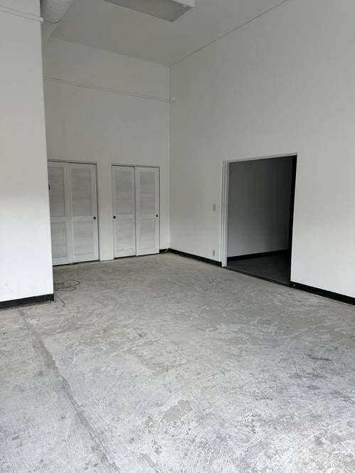 Vacant commercial space with a worn concrete floor, louvered closet doors, and an open doorway.