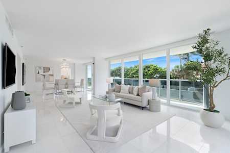 Bright living room with white furnishings and floor-to-ceiling windows overlooking a balcony and greenery.