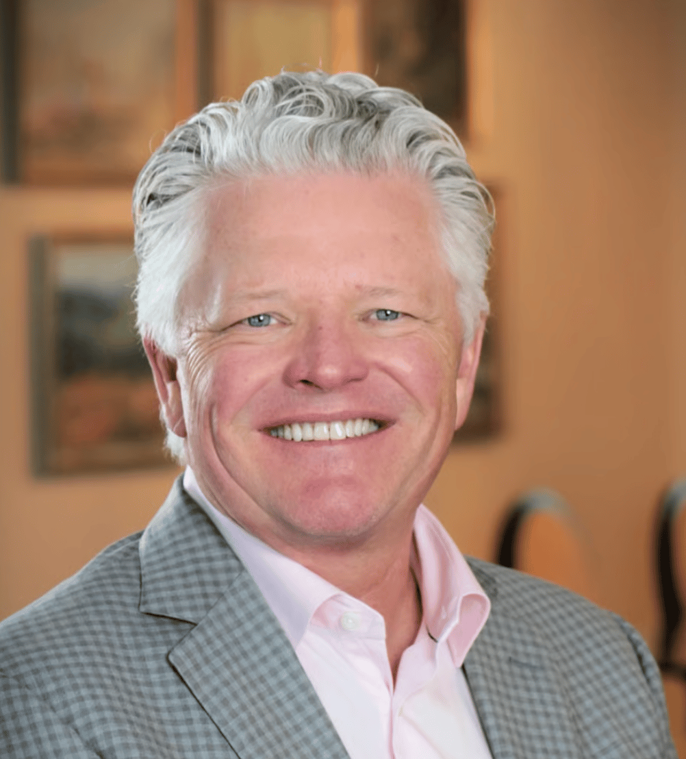 Troy Johnson smiling in a gray checked blazer and pale pink shirt.