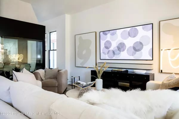 Contemporary living room with white sofas, abstract artwork, and a black media console.