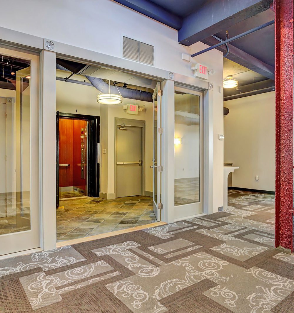Apartment lobby with a red elevator, glass entry doors, and patterned carpet.