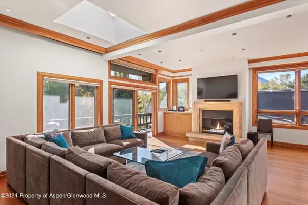 Living room with a taupe sectional, teal pillows, wood-trimmed windows, and a fireplace beneath a television.