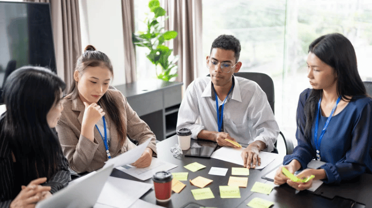 Colleagues meet around a table, reviewing paperwork and sticky notes.