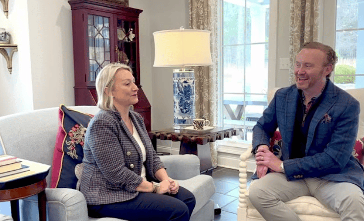 Two adults discuss travel while seated in a bright living room.