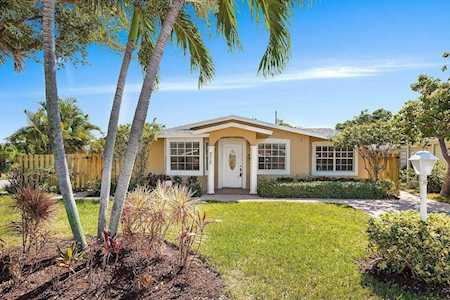 Single-story home with a white front door, broad green lawn, and palm trees.