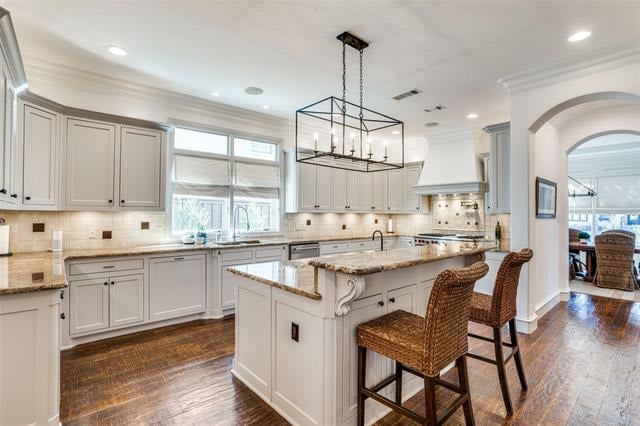 Bright white kitchen with a large stone island, woven bar stools, and dark wood floors.