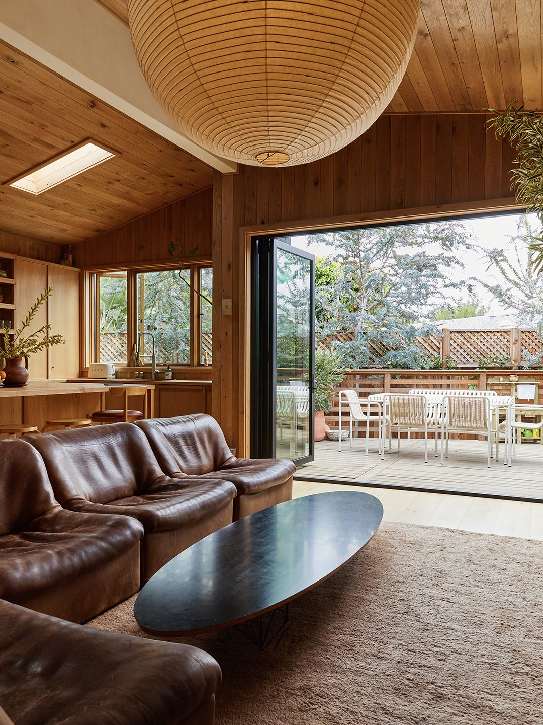A living room with leather sofas around an oval coffee table, sliding glass doors open to a deck and garden.