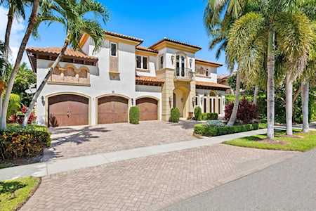 Two-story stucco home with three arched garage doors, a paver driveway, and palm trees.