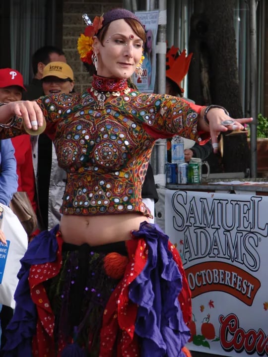 A woman performing a dance in a colorful, mirror-work embroidered top and layered, ruffled skirt at an outdoor festival.