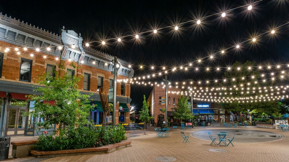 Downtown plaza at night with brick storefronts and rows of string lights overhead.