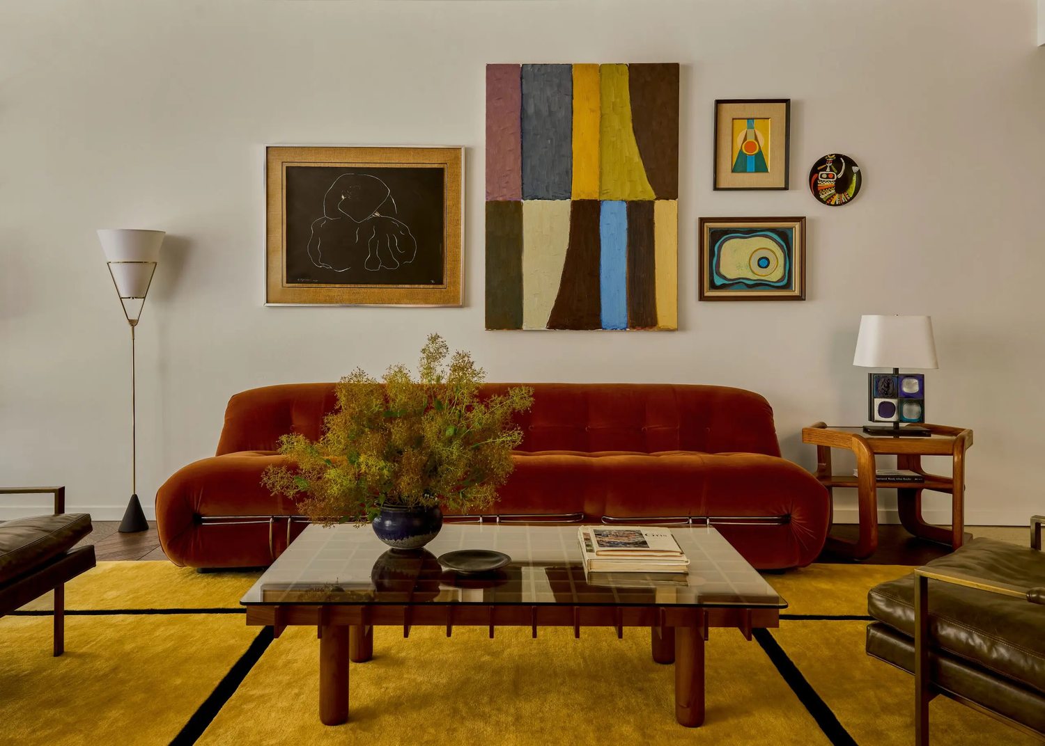 Living room designed by Coco Greenblum with a burnt-orange sofa, layered artwork, and a mix of antique midcentury furniture.