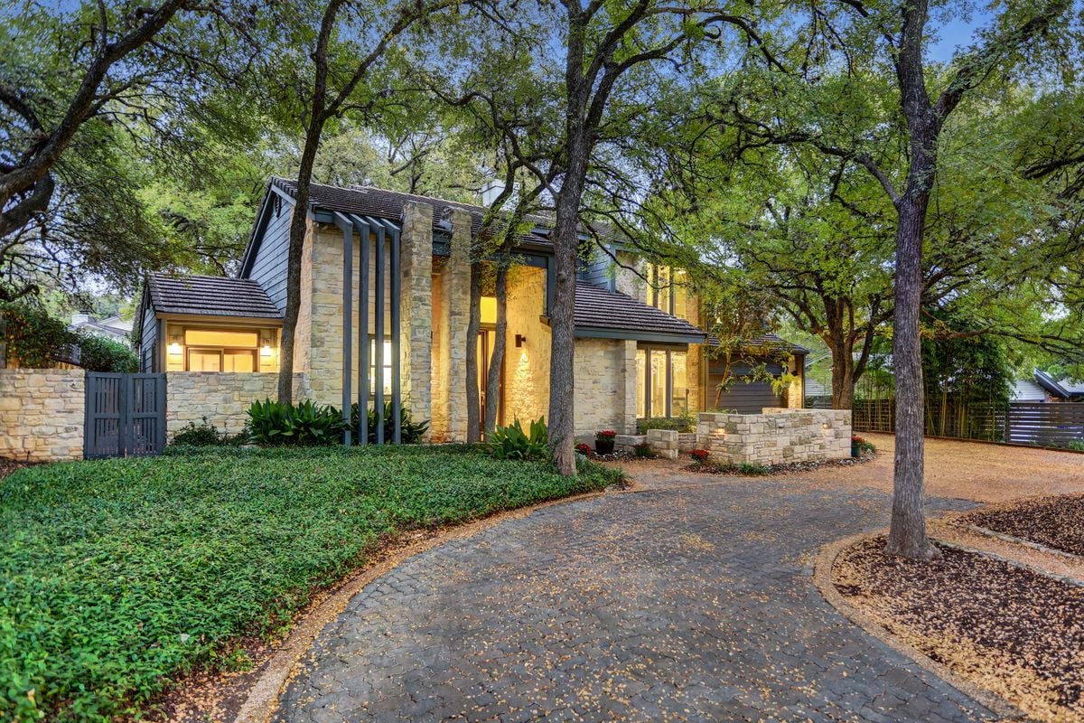 Front elevation of this modern home at 2131 Barton Hills Drive, Austin, TX 78704, showing stone and wood siding accents beneath mature oak trees. Built by Wilde Custom Homes in Barton Hills, near Zilker Park.