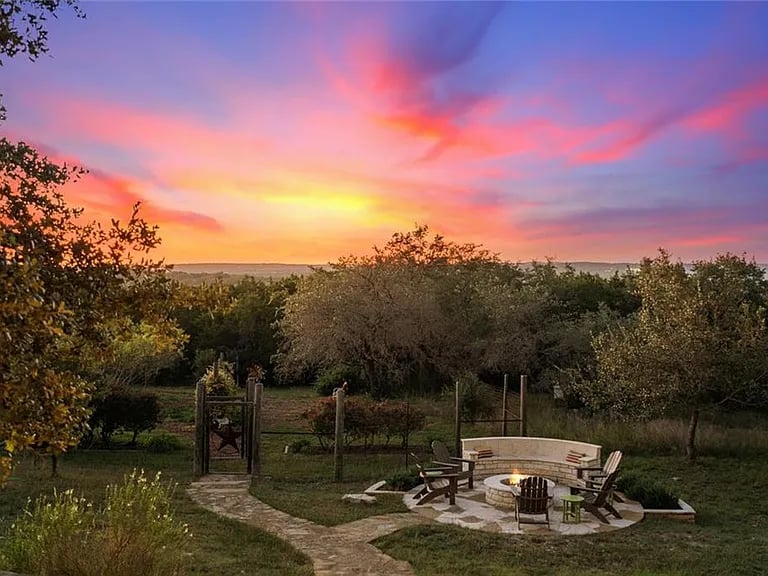 Backyard patio with a fire pit and curved seating beneath a vivid sunset.