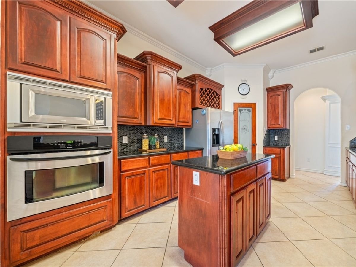 Kitchen at 6825 Island Park Court in Corpus Christi, Texas, featuring custom wood cabinetry, granite countertops, a center island, and stainless steel appliances.