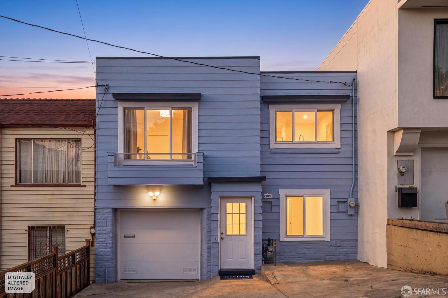 Blue multi-level home with a garage and warmly lit windows at dusk.