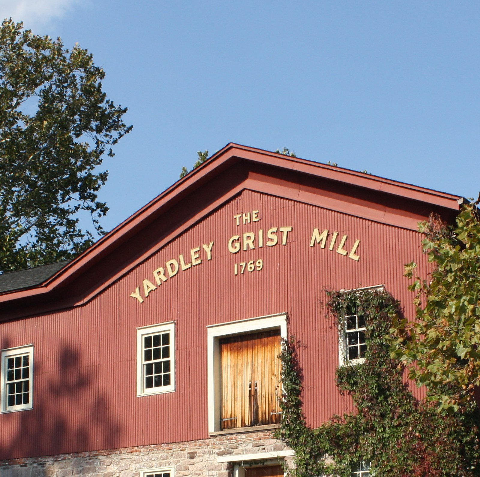 Red gable of the 1769 Yardley Grist Mill with gold lettering under a blue sky in Yardley, PA
