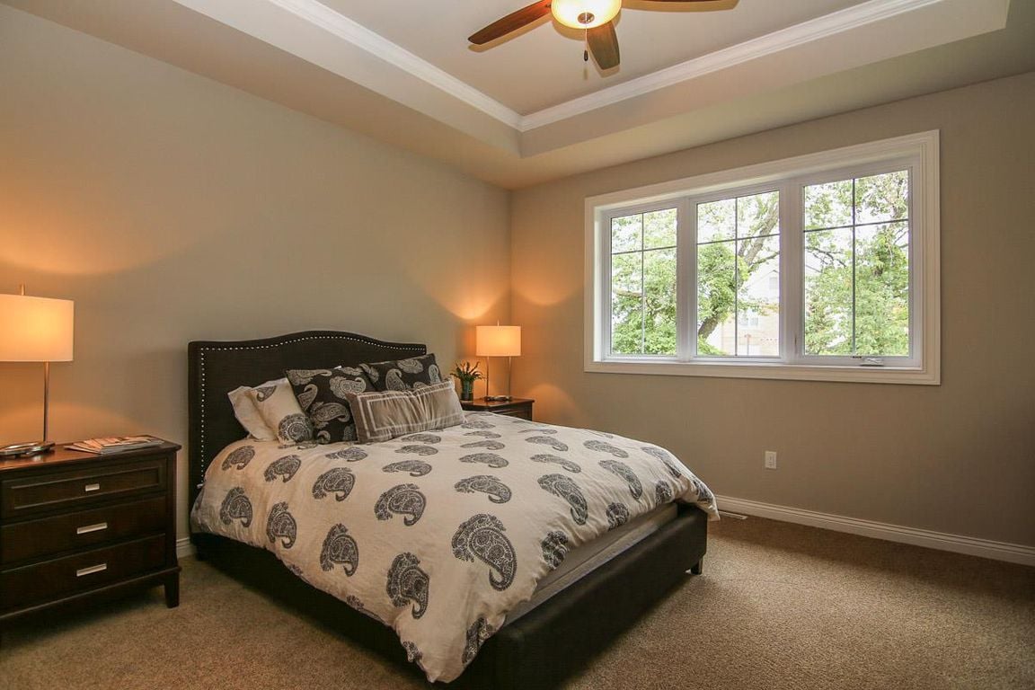 Furnished bedroom with paisley bedding, dark bedside furniture, and a large window overlooking trees.