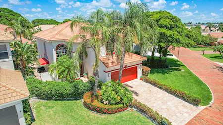 Two-story home with a red garage door, terracotta tile roof, palm trees, and landscaped yard.