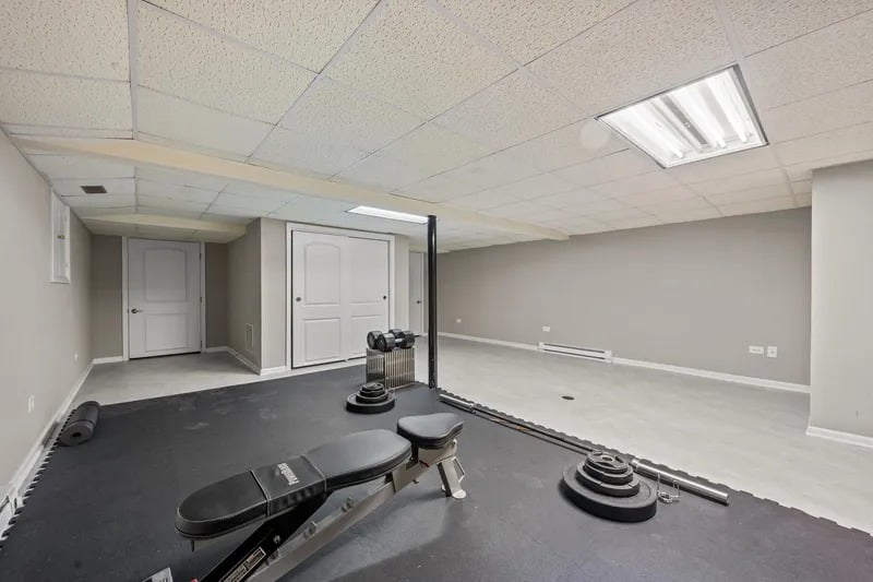 Basement home gym with a weight bench and free weights on black exercise mats.
