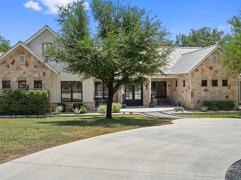 Stone-front home with metal roofs, a large front-yard tree, and a curved driveway.