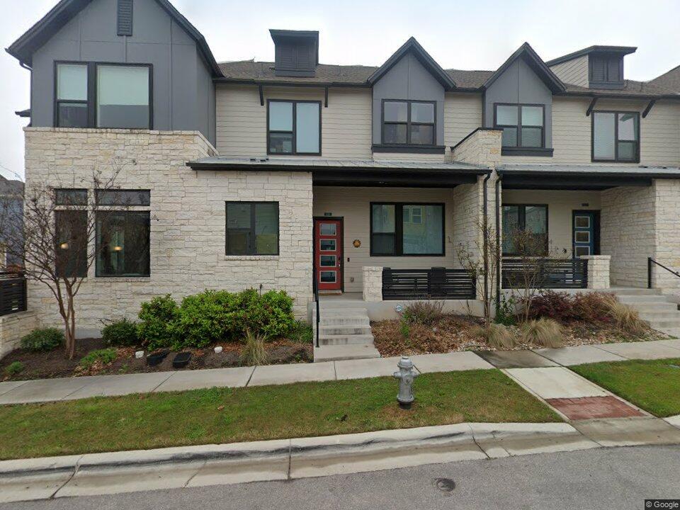 Two-story townhouse with pale stone facade, red entry door, and covered front porch.