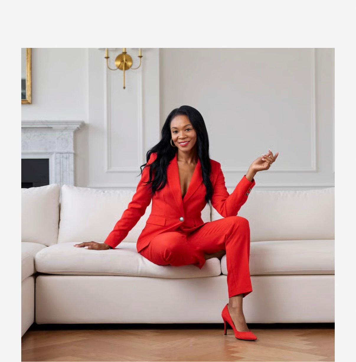 Tonda Booker seated on a white sofa in a bright red suit.
