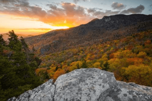 Autumn mountains and forest at sunset, viewed from a rocky outcrop.