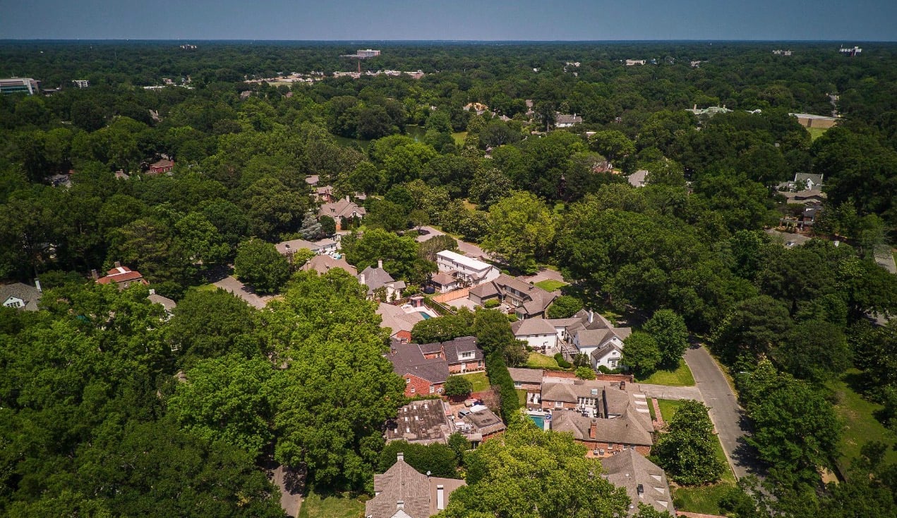 Aerial view of a tree-filled residential neighborhood with homes and a winding street.