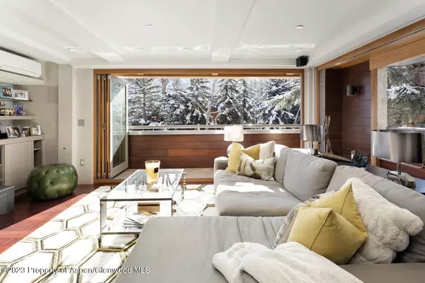 Modern living room with a white sectional and wide windows overlooking snow-covered trees.