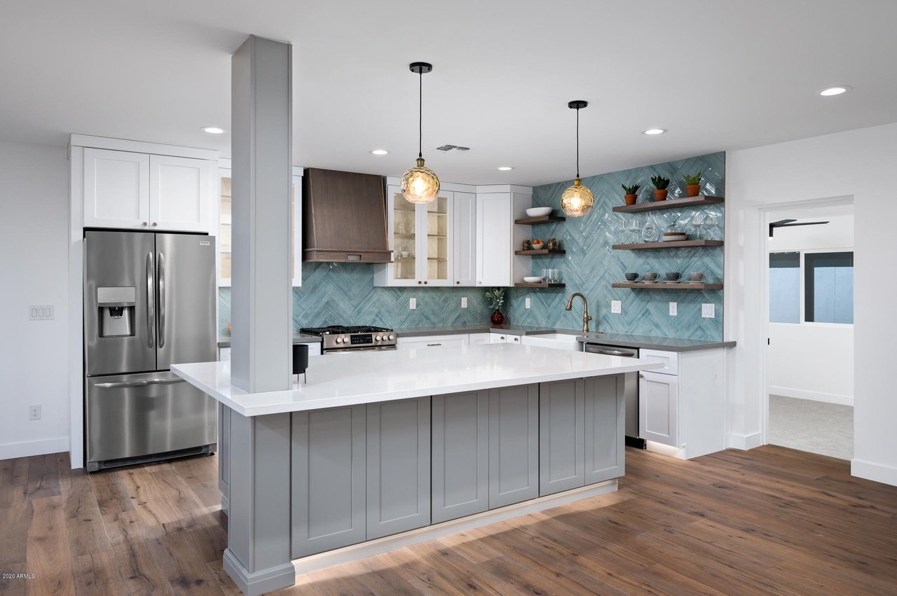 Kitchen with a large gray island, turquoise herringbone backsplash, white cabinets, and stainless steel appliances.