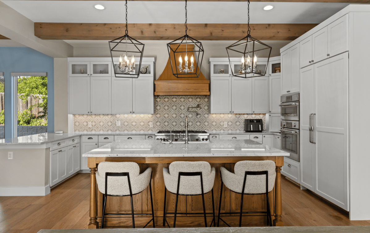 Kitchen with white cabinets, patterned tile backsplash, and a wood-trimmed island with three stools.