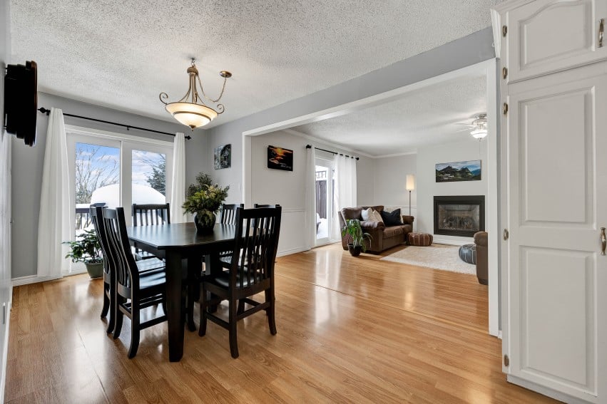 Open dining and living room with hardwood floors, dark dining set, and a fireplace.