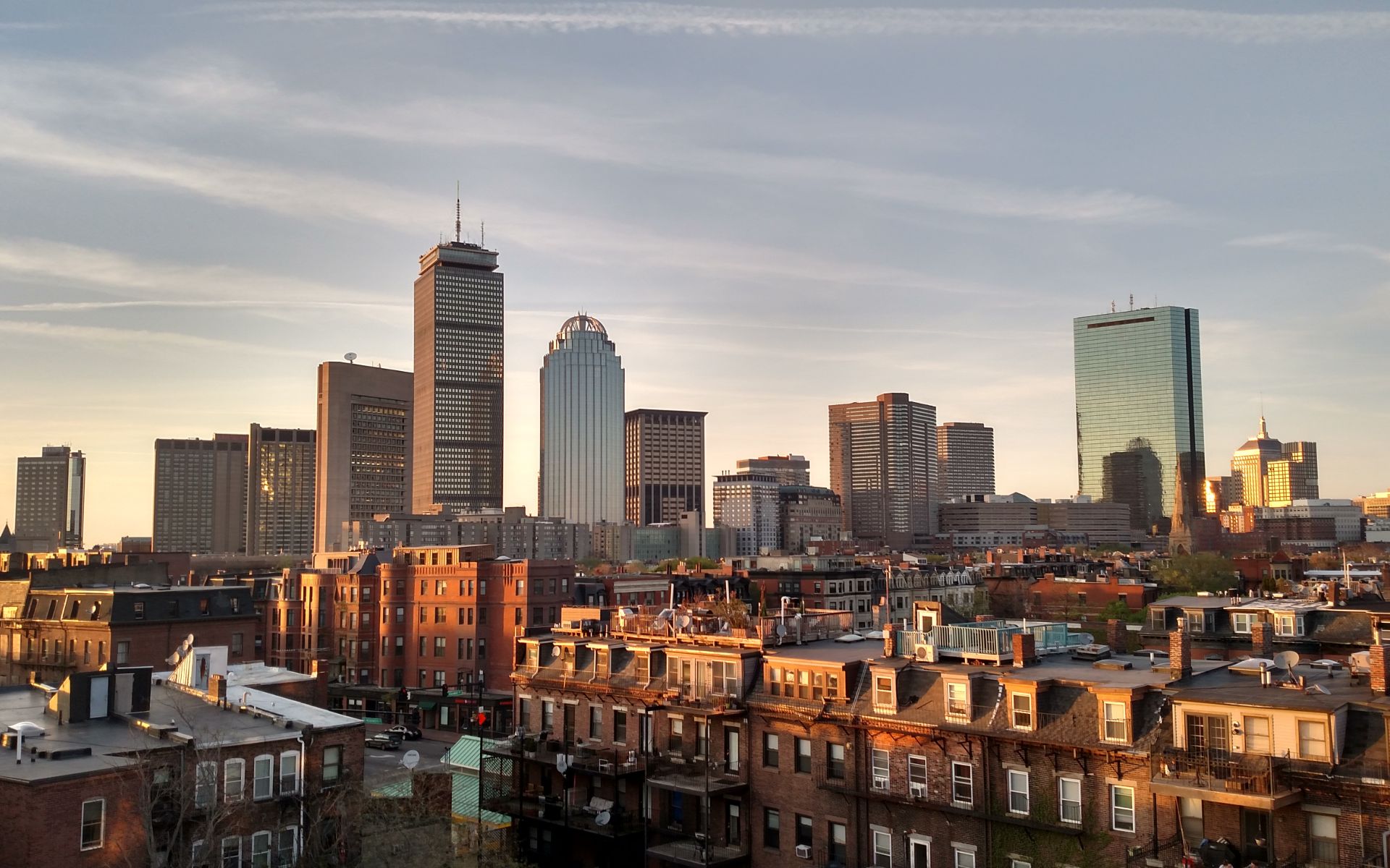 Boston skyline above South End rooftops in warm golden-hour light.
