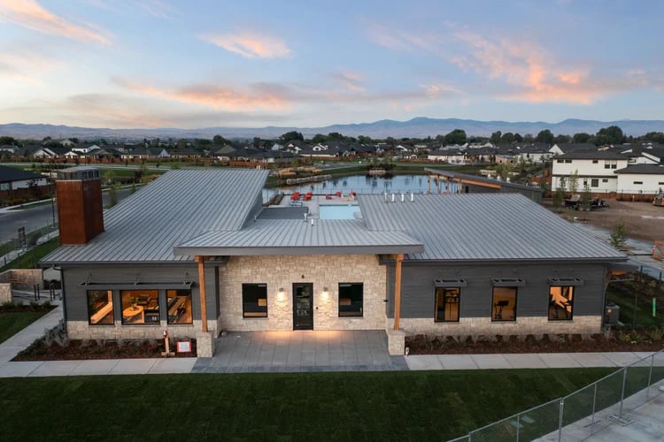 Modern Riverstone community building beside a pond, with homes and mountains in the distance.