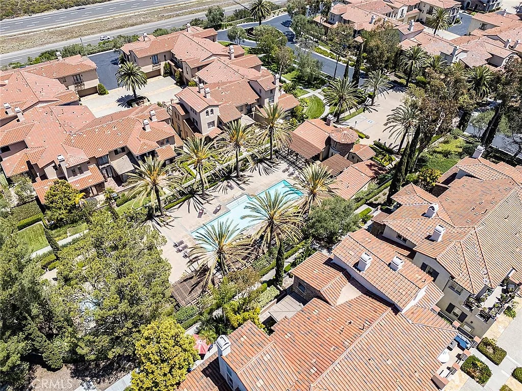Aerial view of a tile-roofed residential community with a central pool and palm trees.