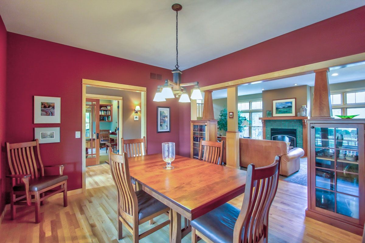 Dining room with a large wooden table, red walls, and an open view into the living room.