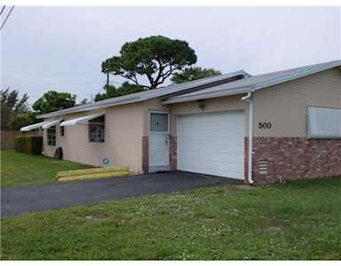 Single-story home with a white garage door, brick facade, and grassy front lawn.