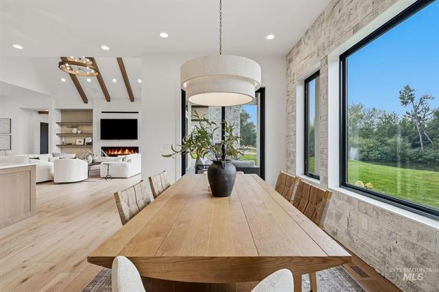 Dining area with a long wood table beside large windows overlooking a green lawn.
