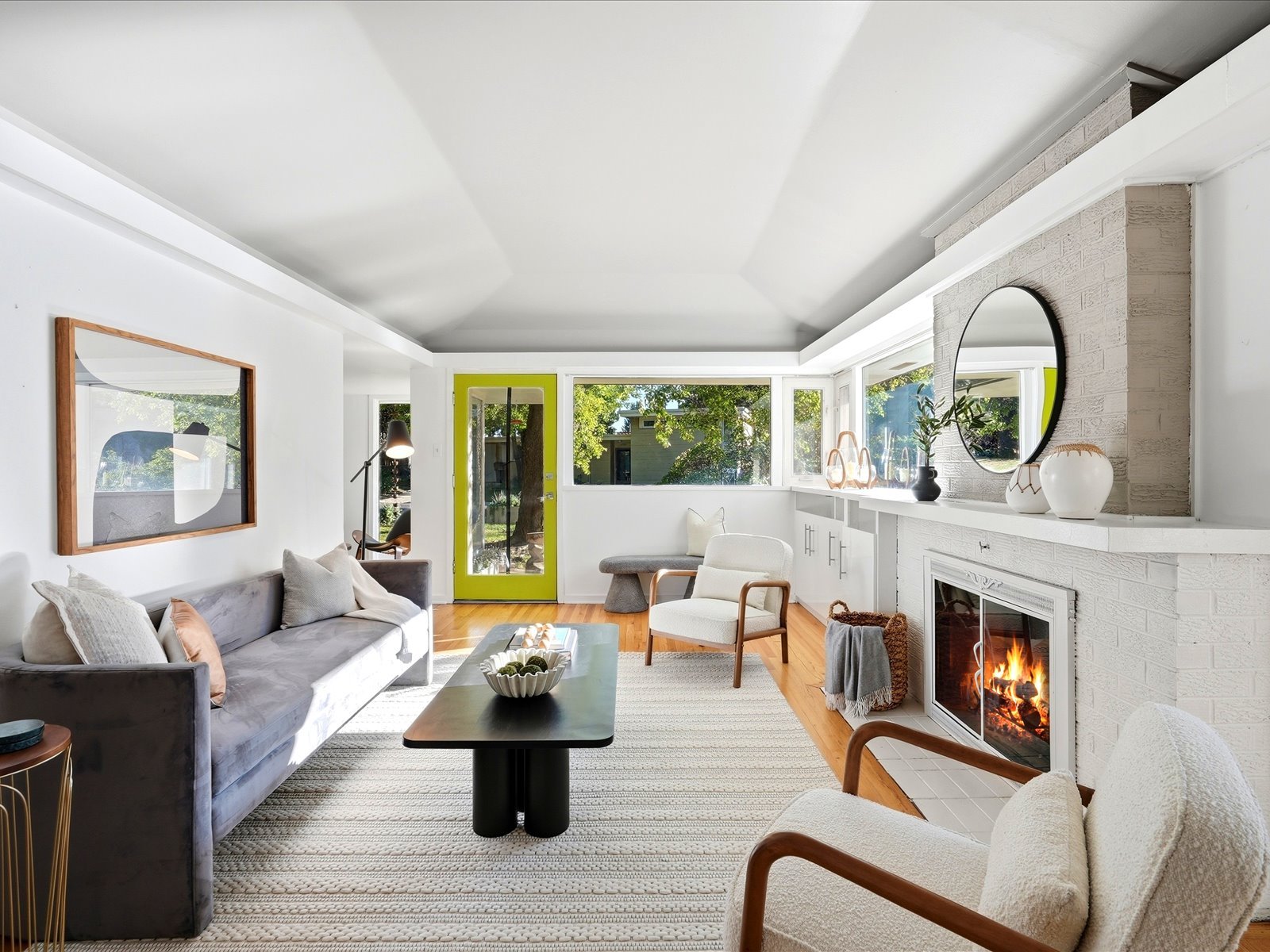 Staged living room with a vaulted ceiling, lime-green door, and white brick fireplace.