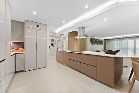 Modern kitchen with a long taupe island, streamlined cabinetry, and a dining area by large windows.