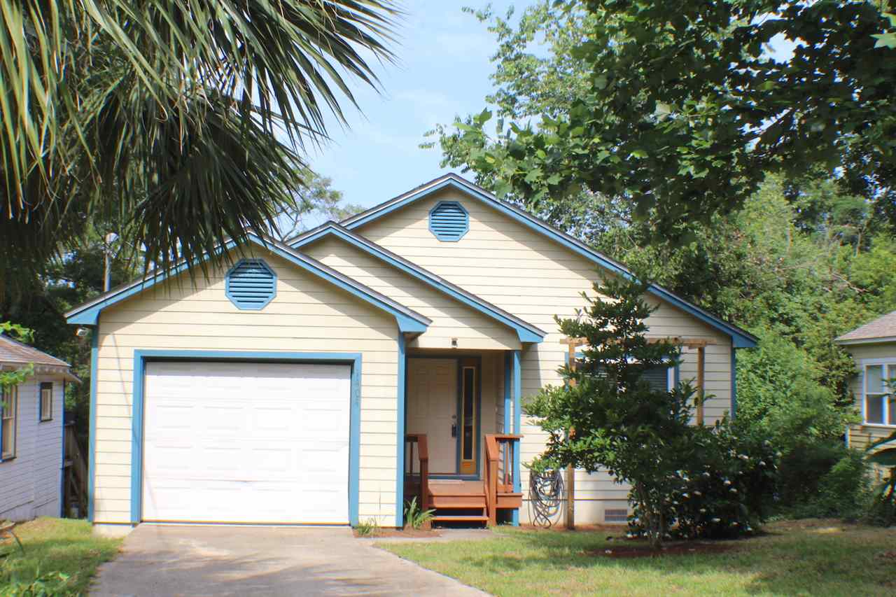 A small house featuring a garage and a driveway, set in a serene residential area.