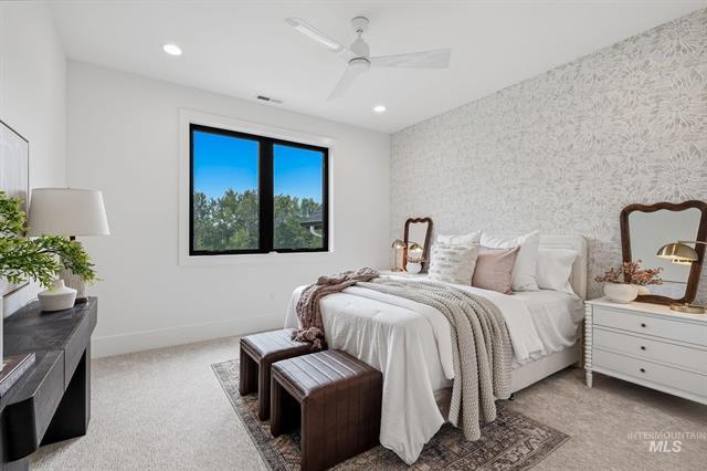 Staged bedroom with a white bed, patterned accent wall, leather benches, and a window overlooking trees.