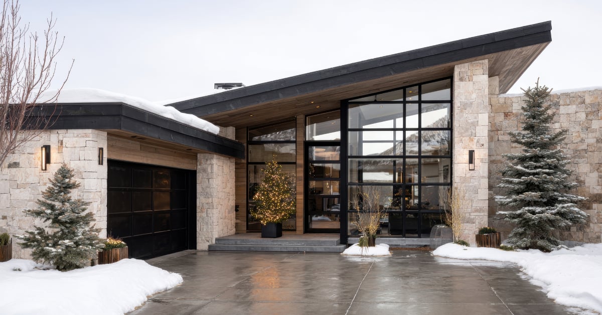 Modern stone and glass home with a clear driveway, lighted entry and subtle winter decor, showing strong curb appeal for a winter sale.