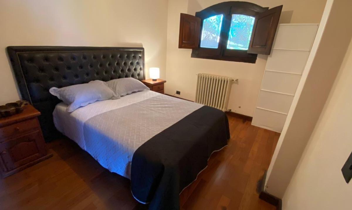 Bedroom with a double bed, dark tufted headboard, wooden floor, and open-shuttered window.
