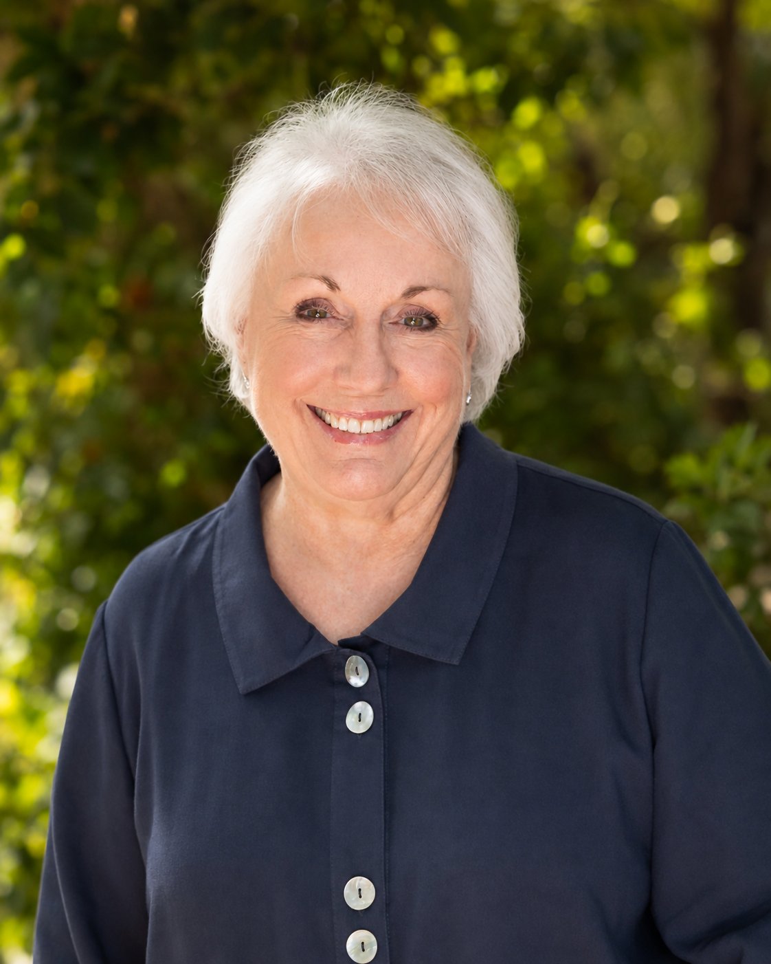 Sherry Hutchens smiling in a navy collared top against leafy greenery.